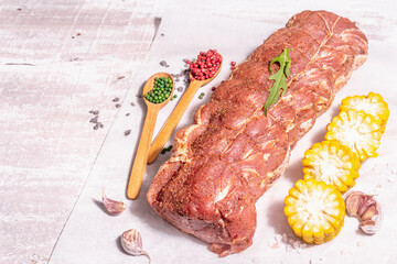 A piece of raw pork loin, marinated fresh meat tied with culinary twine, sweet corn and spices
