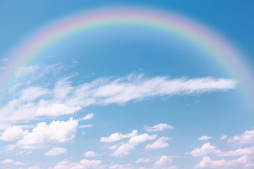 Rainbow over the white clouds on the blue sky 