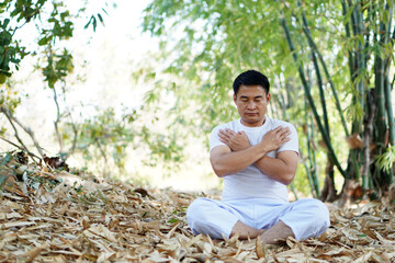 Naklejka na ściany i meble Asian man in white custom sit and do yoga meditation in forest. Concept : Peaceful ,calm, healthy lifestyle and strong soul and body. Relax and recreation activity for happy life.