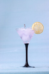 Cocktail glass with ice and lavender lemonade on blue background