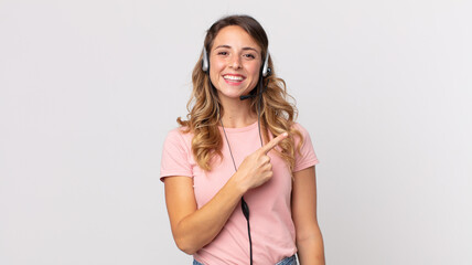pretty thin woman smiling cheerfully, feeling happy and pointing to the side .operator assistant  with a headset - obrazy, fototapety, plakaty