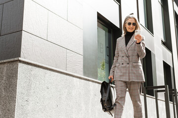 White senior woman using cellphone while walking on street