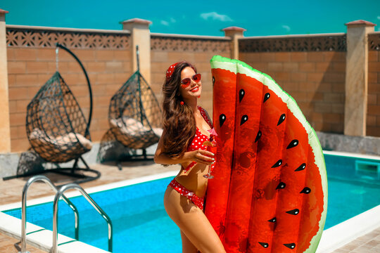 Beautiful woman with watermelon lilo float mattress by swimming pool on villa resort. Sexy bikini girl drink cocktail enjoying summer vacation. Luxury lifestyle and fashion concept.