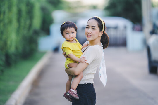 mother holding baby play and learning nature outside with fun emotion with blur village background