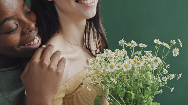 Close up slowmo of African-American woman smiling and hugging her Caucasian girlfriend holding bouquet of daises