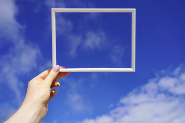 White empty horizontal frame in female hand against blue sky. Sunny day background. Space for your text