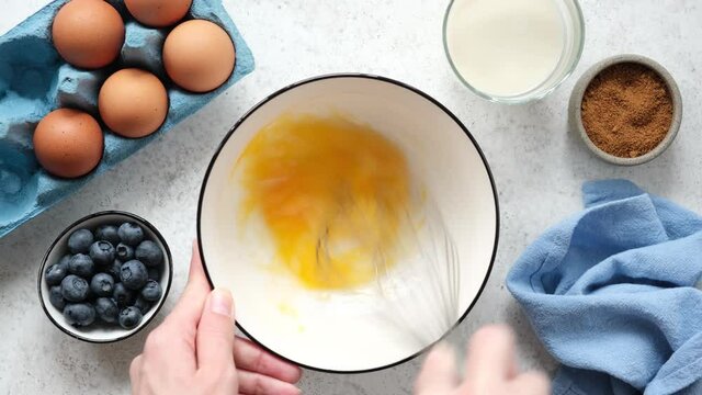 Whisking eggs with wire whisk in a bowl. Female hands cooking top view