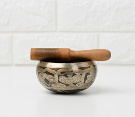 Tibetan singing copper bowl with a wooden clapper on a white wooden table, objects for meditation...