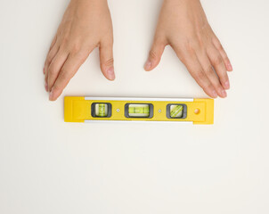 female hands holds a yellow plastic building level on a white background
