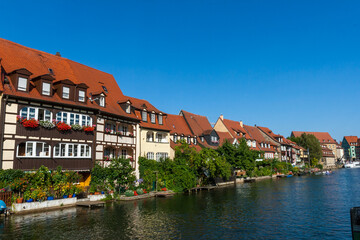 Fototapeta na wymiar Bamberg Germany 08-08-2019 - Picturesque view of the medieval buildings along the Regnitz River with old barge, moored boats and on the river shore in UNESCO Heritage city Bamberg, Bavaria, Germany.