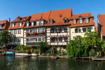 Fototapeta na wymiar Bamberg Germany 08-08-2019 - Picturesque view of the medieval buildings along the Regnitz River with old barge, moored boats and on the river shore in UNESCO Heritage city Bamberg, Bavaria, Germany.