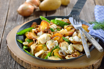 Deftiges Fischgröstl mit Bratkartoffeln, Heilbutt und Zuckerschoten - Fried potatoes with pieces of halibut fillet, sugar peas and onion rings, often served in a frying pan