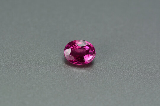 Natural earth mined unheated, untreated oval faceted rich red color loose small ruby gemstone setting for making jewelry from Winza, Tanzania. Gray patterned backgound. Gemology, mineralogy  theme.