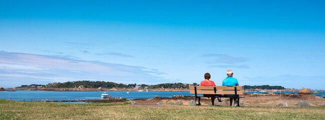 Fototapeta na wymiar couple on bench looks at ferry to ile de brehat in french brittany