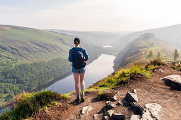 Female hiker enjoying the view from The Spinc trail over Glendalough Upper Lake on a hazy summer...