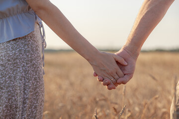 Love concept. A couple holding hand during sunset, a symbol of love and happy relationship. A young couple in love walks through a Wheat field at sunset, holding hands and looking at the sunset