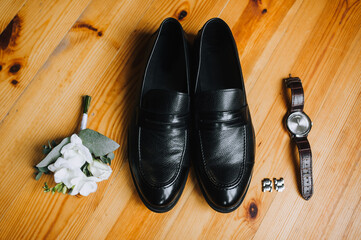 Wedding accessories and details of the groom on the background of wooden parquet, top view: black shoes, boutonniere, wrist watch, cufflinks.