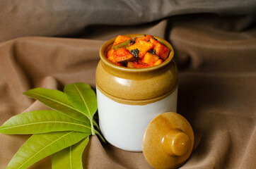 Homemade raw mango pickle in a traditional ceramic jar on Brown background