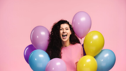 Fototapeta na wymiar overjoyed woman with plenty of multicolored balloons isolated on pink