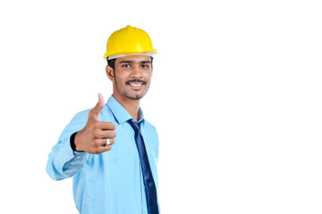 Young Indian engineer wearing yellow color hard hat and giving successful gesture.