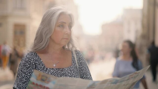 Middle aged lady walking down the street, looking for way using paper map in old town. Attractive senior tourist getting lost in big city trying to find route. 