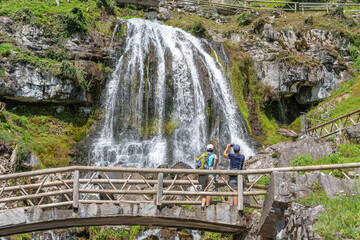 Hikers at the waterfall in front of the St. Beatus Caves near Beatenberg