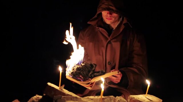 a man in a cloak with a hood is reading a hot book with candles on the floor, the shaman is performing a ceremony before halloween