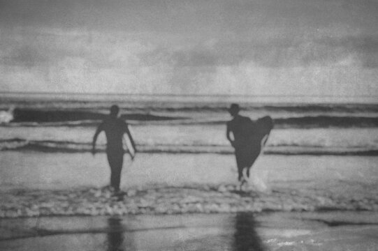 Silhouette Of surfers carrying their surfboard into the sea, vintage filter effect with blurred edit