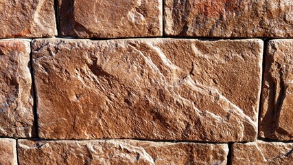 a fragment of masonry from a natural stone of a brown shade with an uneven relief texture, a rough dark background of the joints of decorative stone tiles, stone blocks in the exterior design