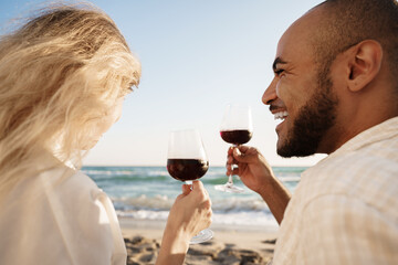 Portrait of a young couple sitting on the beach and drinking wine