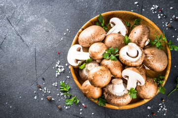 Raw mushrooms Champignon in wooden bowl with spices. Top view at black background.