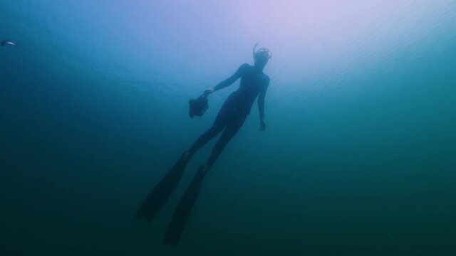 Underwater photographer. Woman swims underwater with professional camera housing in the freshwater lake and enjoys the underwater world around her full of weed and fish