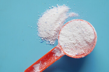 Washing powder in plastic spoon on blue background 