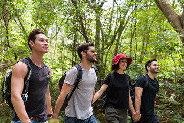 Group of male and woman backpackers hikers hiking with backpacks walking on road along forest trial. Camping, jungle adventure concept
