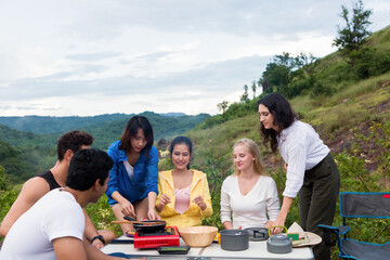 Group of diverse young tourist friends camping, cooking on mountain. Group of young traveler women cooking together while group of young men pitching tent on camping holiday