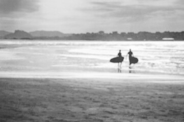Silhouette Of surfers carrying their surfboard into the sea, with a vintage filter, blurred edit