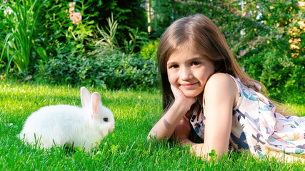 A beautiful girl lies on the lawn and plays with a baby bunny. Decorative dwarf rabbit eating grass...