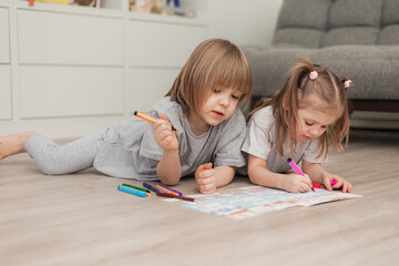 two small children boy and girl lie at home on a wooden floor and draw. High quality photo