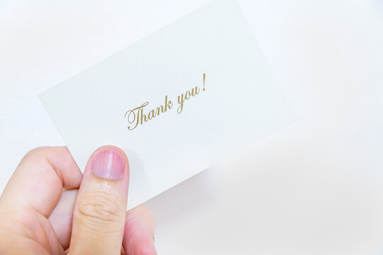 「Thank you」と書かれたメッセージカードを持つ人の写真。感謝を伝えるイメージ。