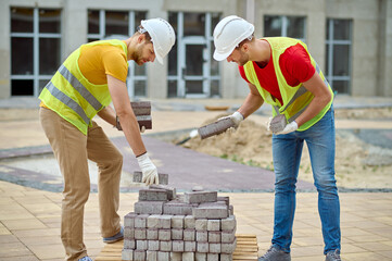 Skilled builders in cotton gloves choosing construction materials for pavement