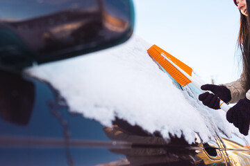 Woman cleans car with a brush from snow after a blizzard