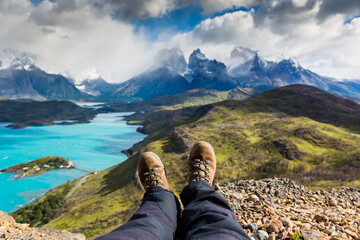 Naklejka premium Legs of traveler sitting on a high mountain top in travel. Freedom concept. Los Cuernos rocks, Patagonia, Chile