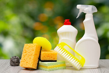 Bottles of dishwashing liquid, glass and tile cleaner and sponges on blurred background.