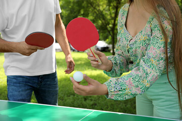 Couple with tennis rackets and ball near ping pong table in park, closeup