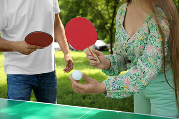 Couple with tennis rackets and ball near ping pong table in park, closeup