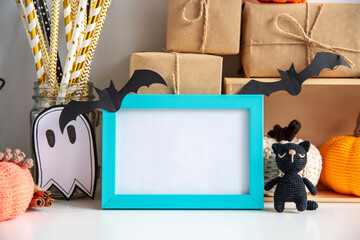 Halloween decor on a white background with a frame with empty space. Knitted pumpkins, witch hat, kerasin lamp, gifts in craft paper, blue frame.