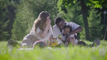 Black father, fair-skinned mother and mestizo child in the park. Happy family on a picnic in the park. Joyful