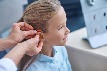 Doctors hands trying on hearing aid to girl