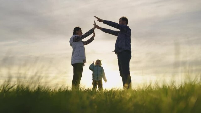 Happy family playing with little daughter, family symbol at home in sun. Mom, dad and they depict with their hands roof of house over head of child. Dream of a shared home. Home builders