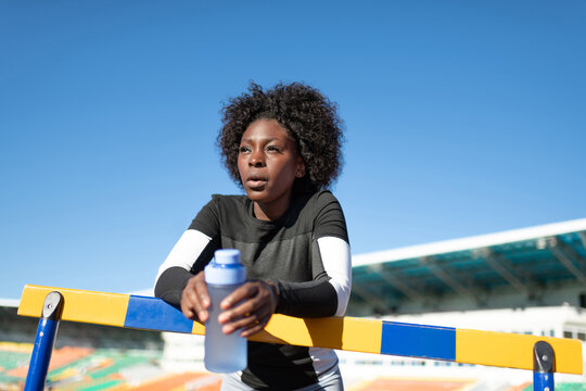 Black sportswoman with water resting near barrier